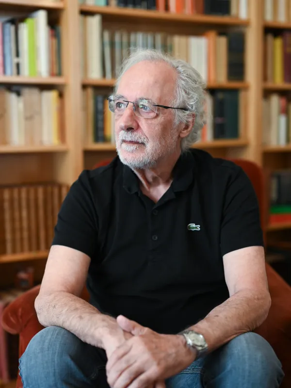 Pierre Agostini seated with blurred bookshelf behind him