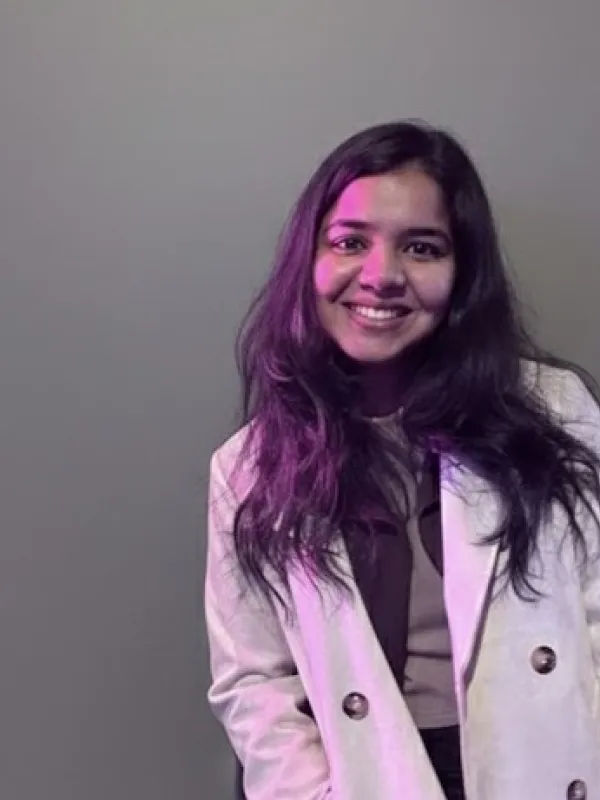 Headshot of Aiswarya Amalucottage smiling in a white coat against a gray background