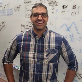 Professor Singh smiling with hands on hips in front of a whiteboard